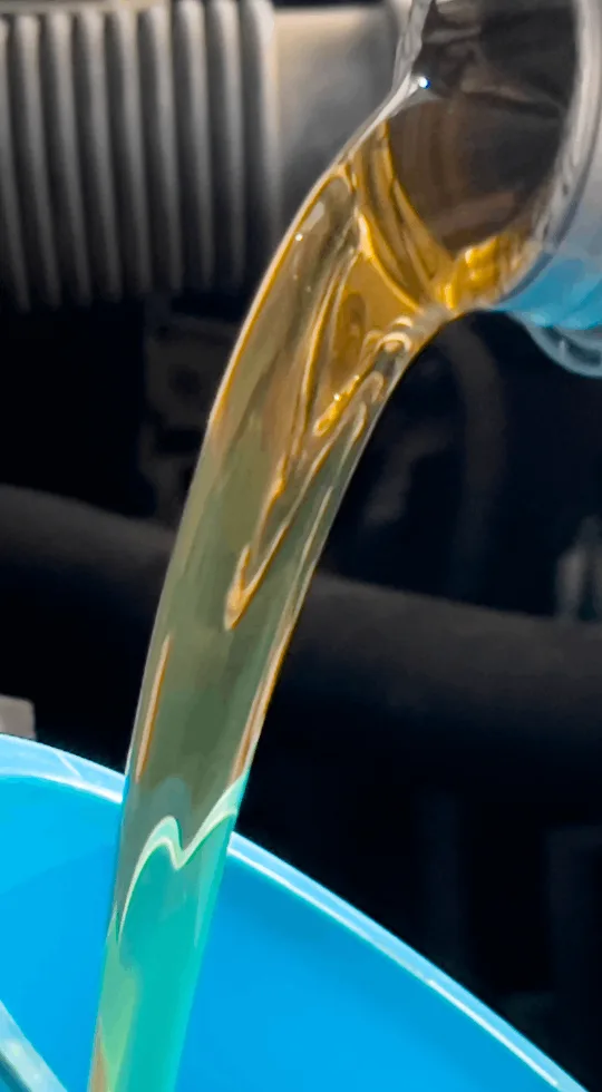 Pouring golden motor oil into a blue container, engine background visible.