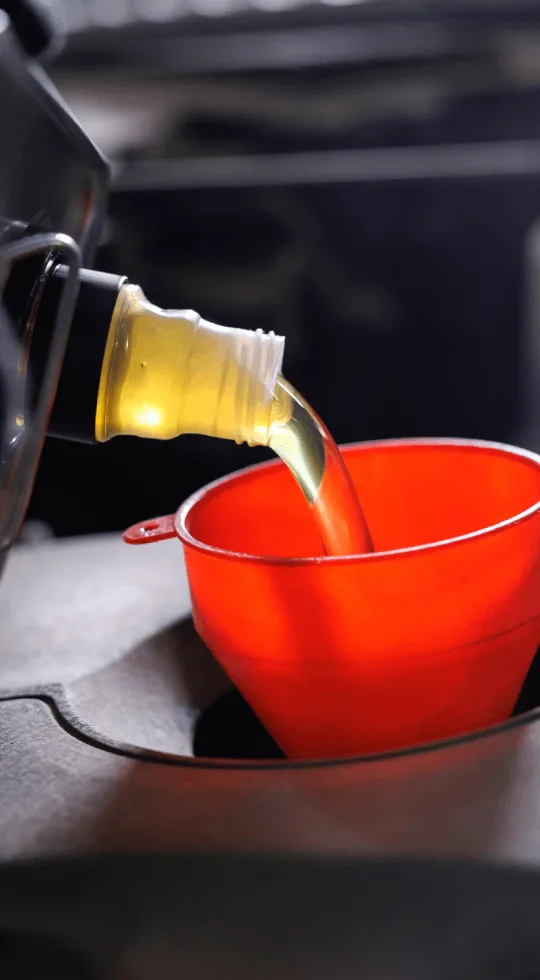 Pouring oil into a red funnel during a car maintenance.