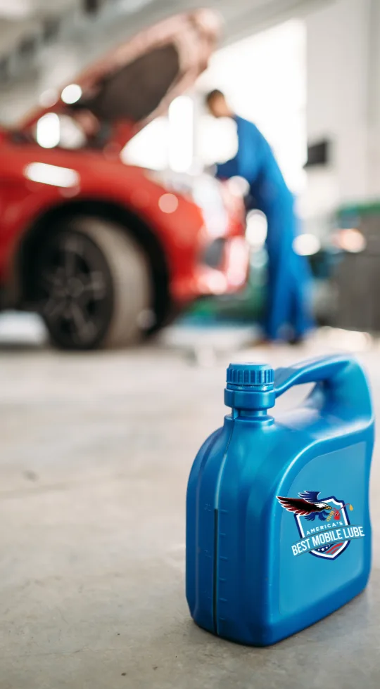 Blue oil container in focus, with a mechanic working on a red car in the blurred background.